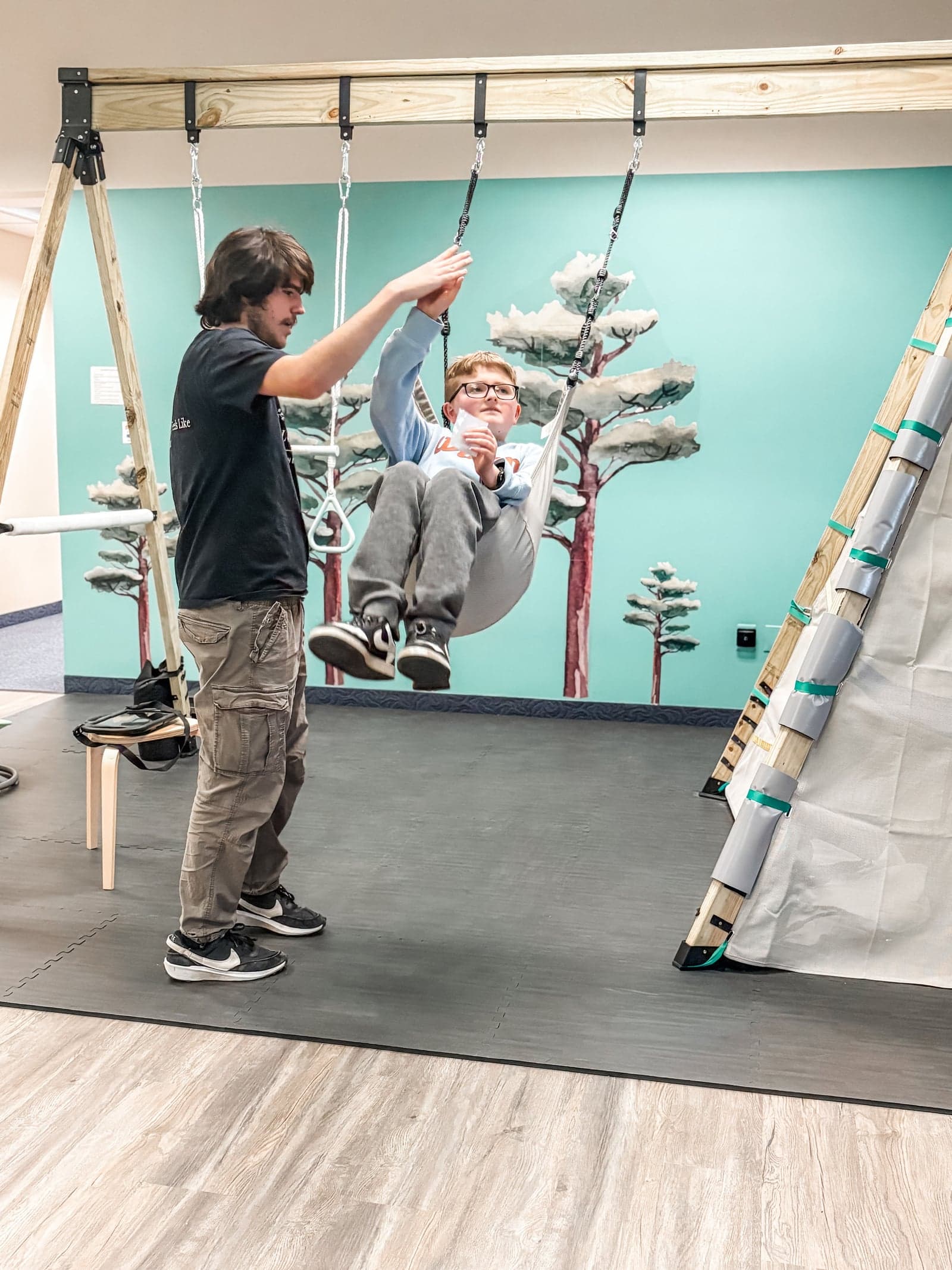 Therapist pushing child on swing in therapy gym